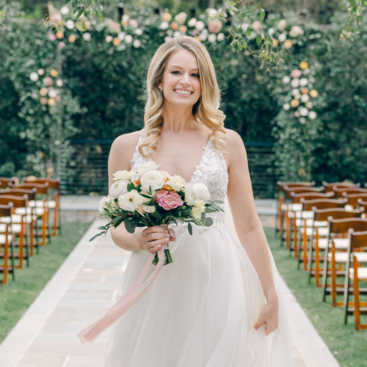 A bride smiling with a flower bouquet in-hand, walking down the aisle at a garden wedding venue in Leesburg, Virginia.