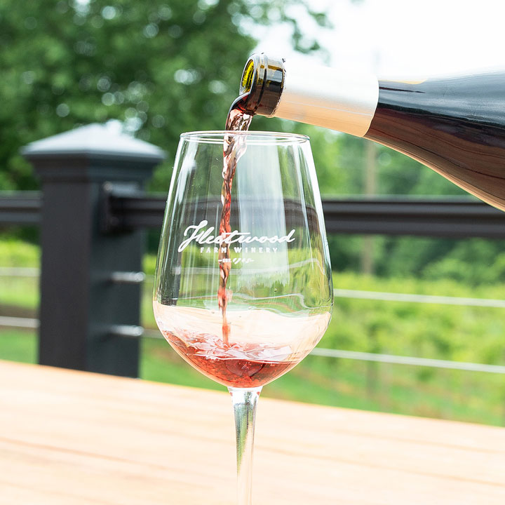 A close-up of red wine being poured into a Fleetwood Farm Winery stem wine glass, overlooking the Loudoun County winery.