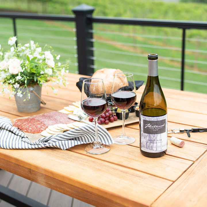 A bottle of Fleetwood Farm Winery red wine with two glasses and a charcuterie board on a wooden table, showcasing Fleetwood as a winery with wine and food.