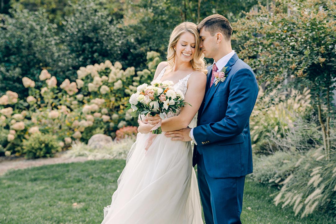 A bride smiling with her groom in front of a garden area at a winery wedding venue in Northern Virginia.