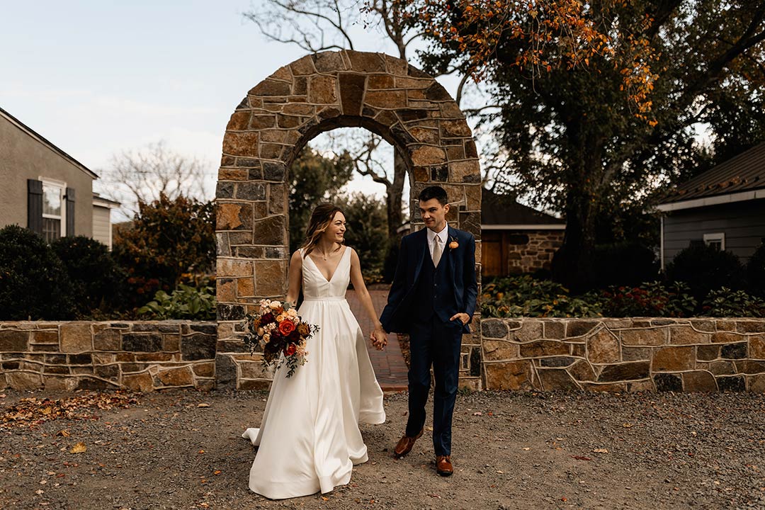 A bride and groom walking in front of a brick archway at a fall wedding venue in Northern Virginia.