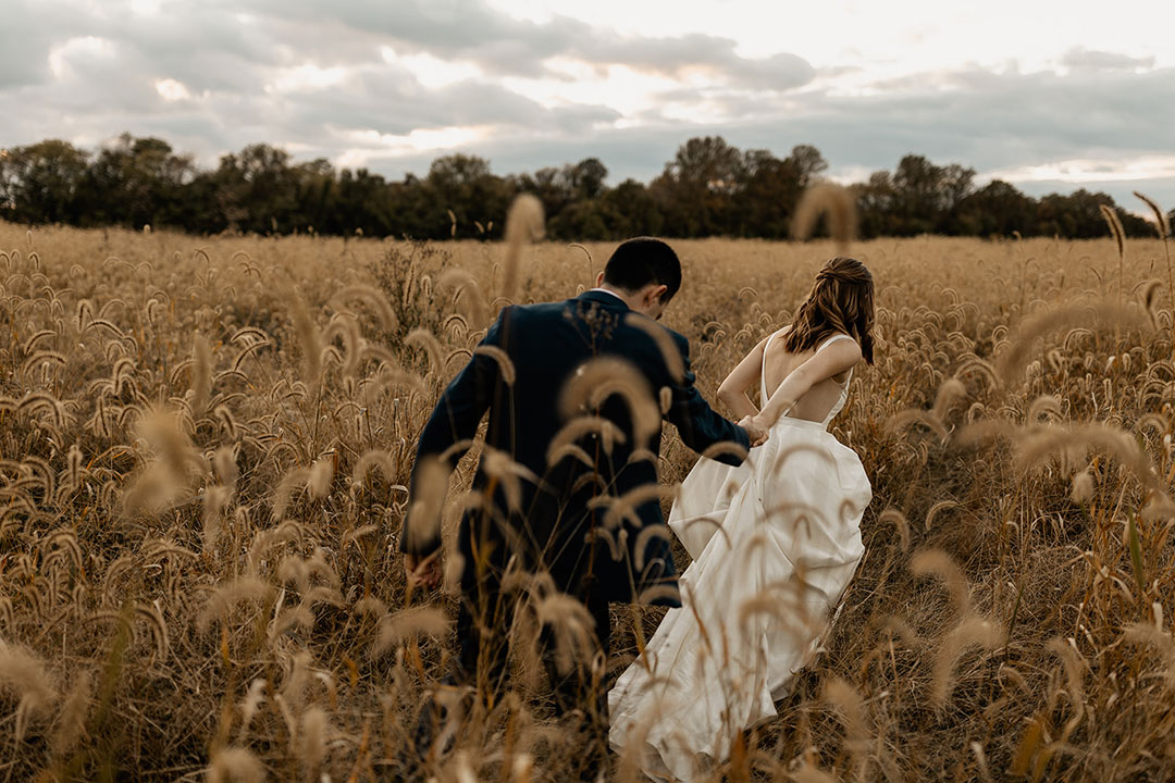 A bride leading a groom through a field of tall grass at a garden wedding venue in Loudoun County, Virginia.