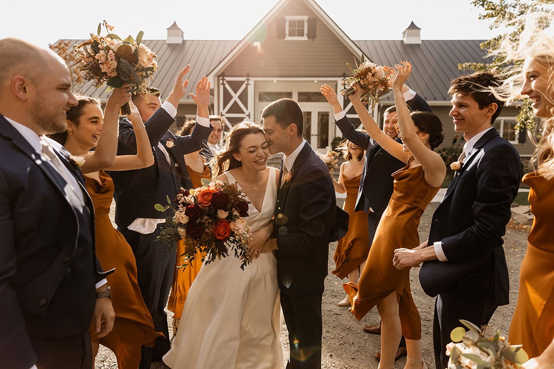 Bridesmaids and groomsmen holding their hands up in celebration of a bride and groom in the center of them at a modern farm wedding venue in Leesburg, VA.