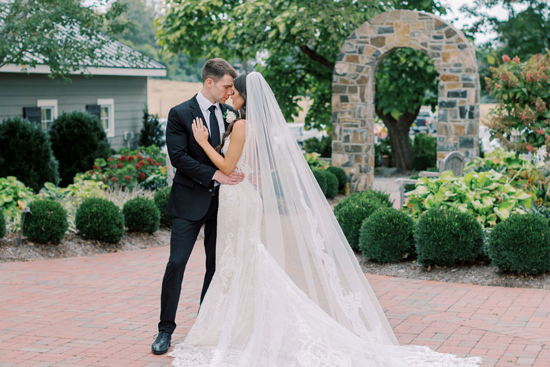 A bride and groom face-to-face, touching foreheads outside a garden area at a garden wedding venue and winery in Virginia.