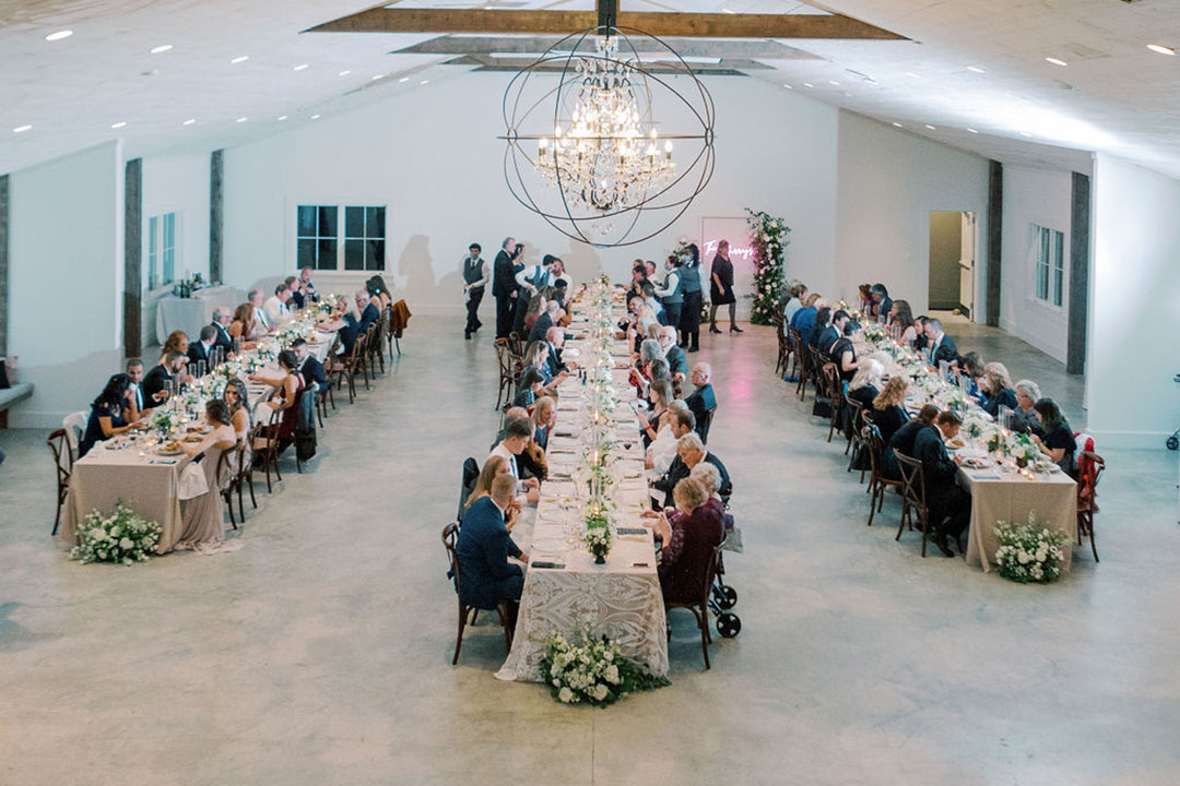 Three rows of tables lined with people enjoying a wedding dinner inside a fall wedding venue in Leesburg, Virginia.