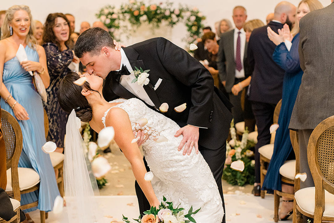 A groom dipping a bride as they share a kiss at their wedding ceremony taking place at a winery wedding venue called Fleetwood Farm Winery.