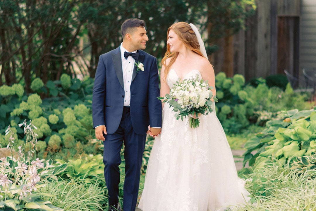 A bride and groom looking at one another, holding hands as they walk around a garden wedding venue in Leesburg, Virginia.