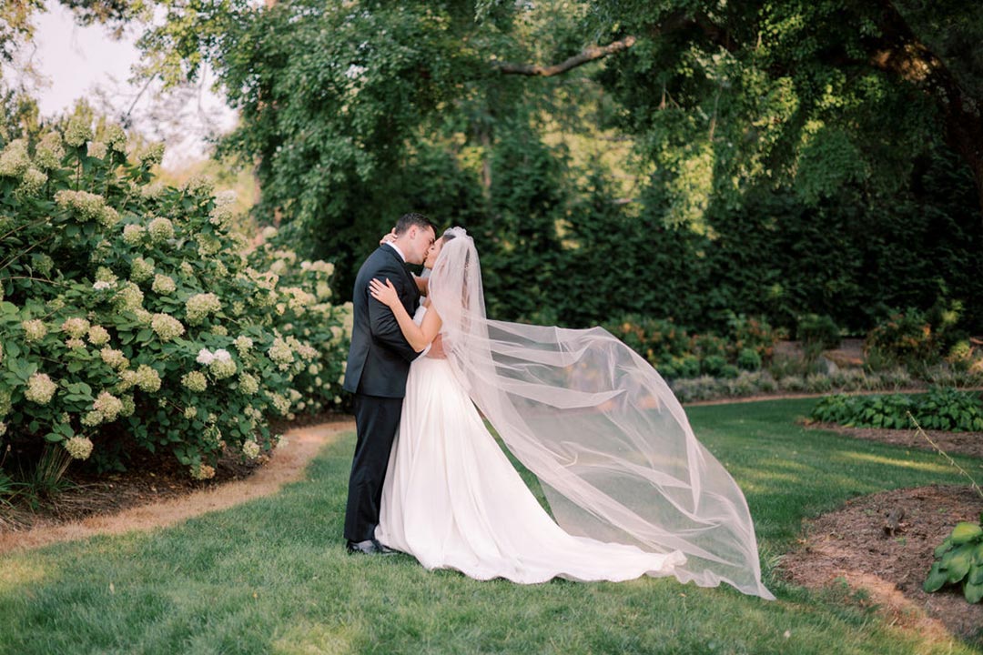 A bride and groom kissing in a garden area outside at a Virginia winery wedding venue called Fleetwood Farm Winery.