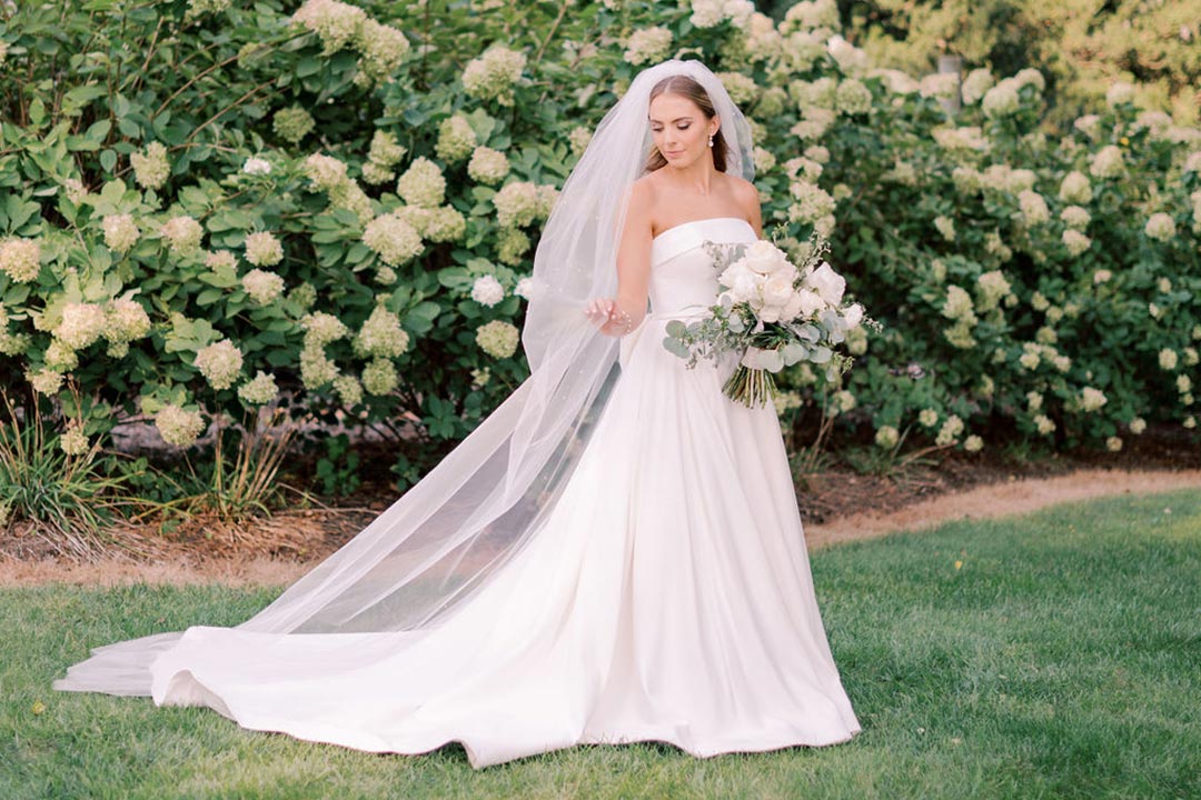 A bride holding flowers in one hand and her veil in the other outside at a Virginia winery wedding venue.