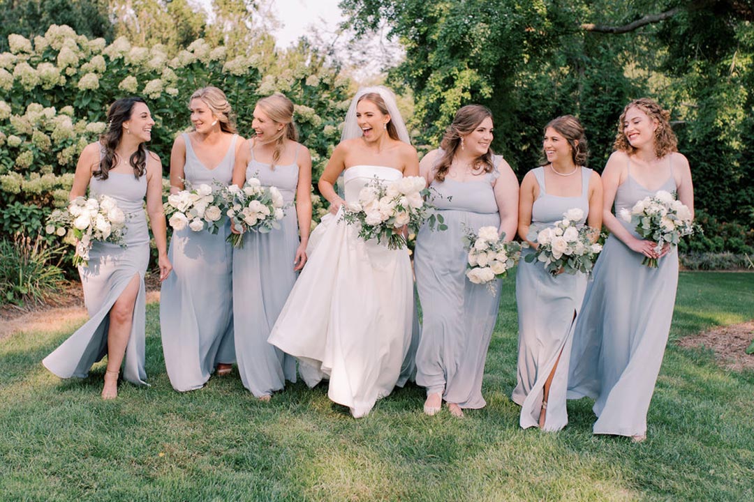 Six bridesmaids and a bride smiling at one another outside a winery wedding venue in Loudoun County, Virginia.