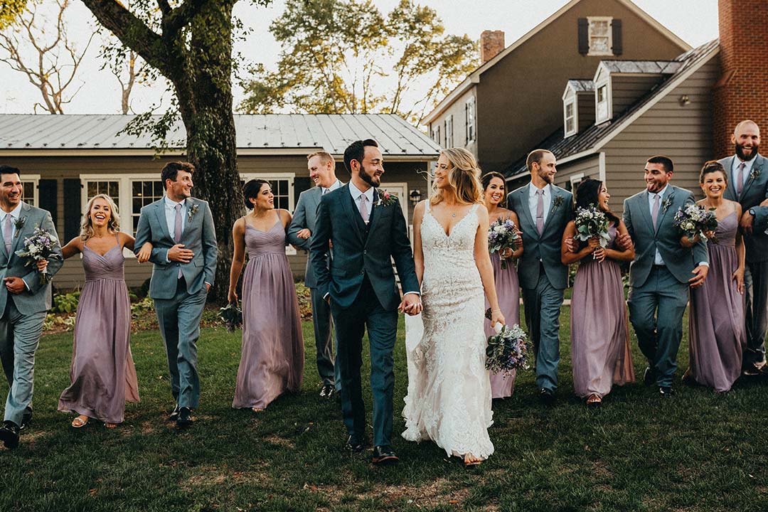 A bride and groom smiling with their bridesmaids and groomsmen lined up behind them at a garden wedding venue in Northern Virginia.