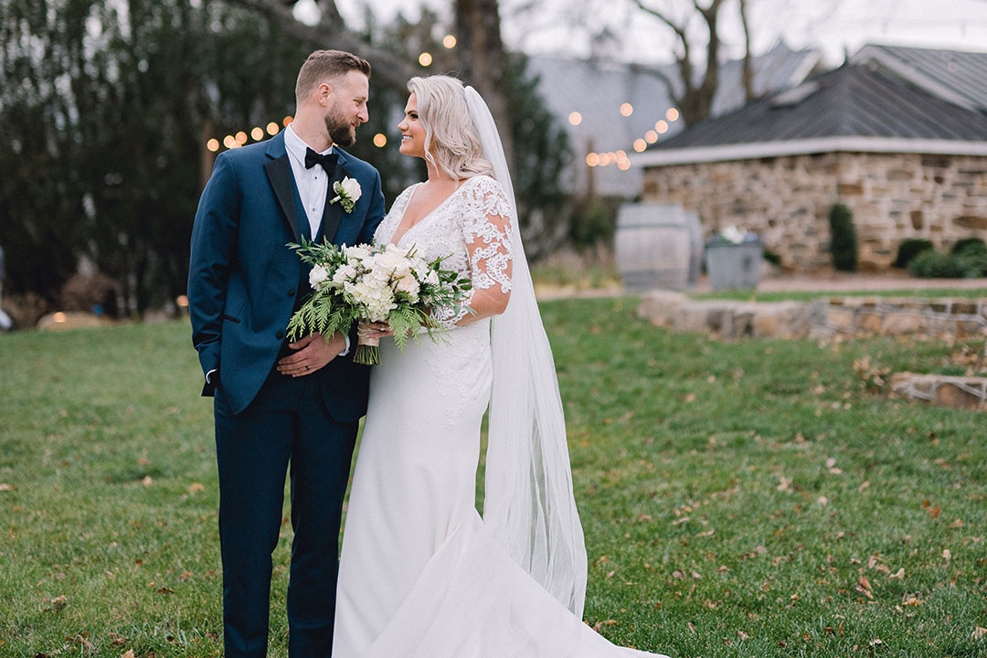 A bride and groom smiling, looking into each other's eyes in a grassy area at Fleetwood Farm Winery, a Leesburg wedding venue.