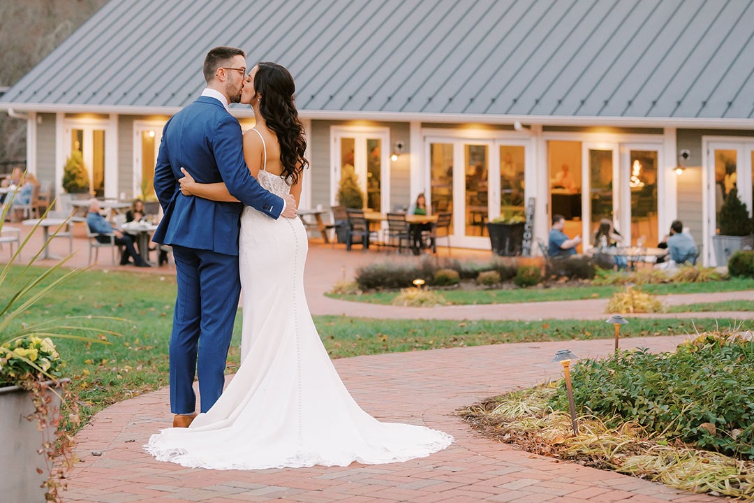 A bride and groom kissing outside along a brick walkway at Fleetwood Farm Winery, an outdoor wedding ceremony venue in Leesburg, Virginia.