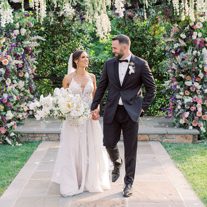 A bride holding hands with her groom, walking down the aisle of an outdoor winery wedding venue in Leesburg, VA.