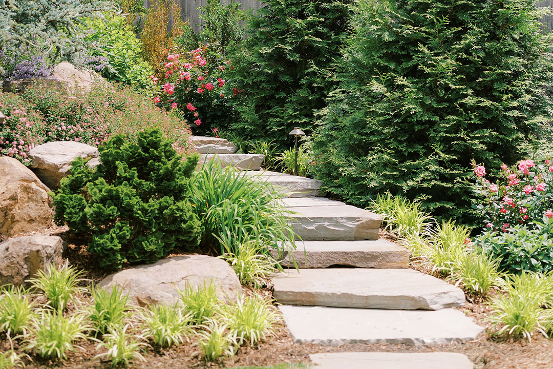 A stone walkway surrounded by flowers and bushes at a Leesburg winery named Fleetwood Farm Winery.