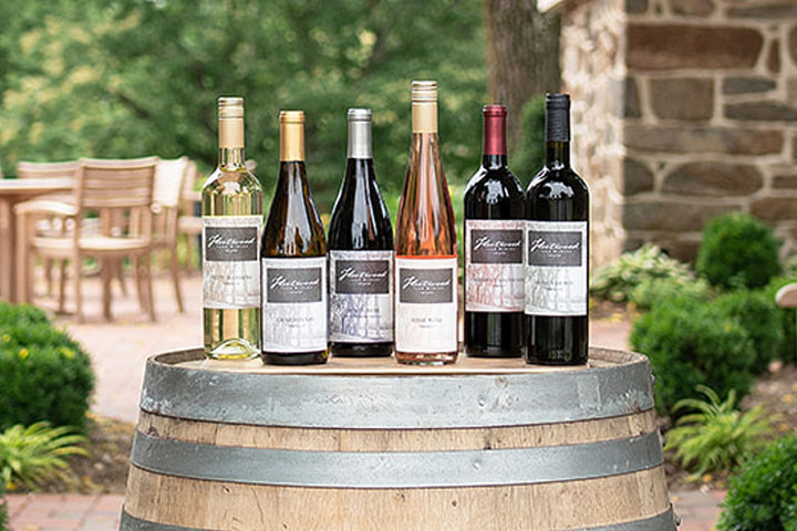 Six bottles of Fleetwood Farm Winery wine lined in a row on a wooden barrel at an outdoor winery in Virginia.