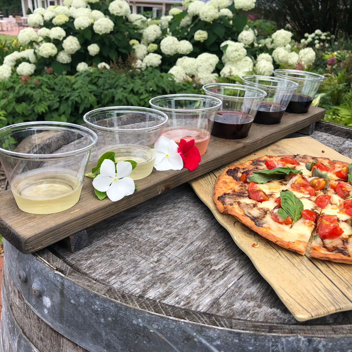 A flight of six different wines lined up on a board next to a flatbread pizza at a winery with live music in Loudoun County, Virginia.