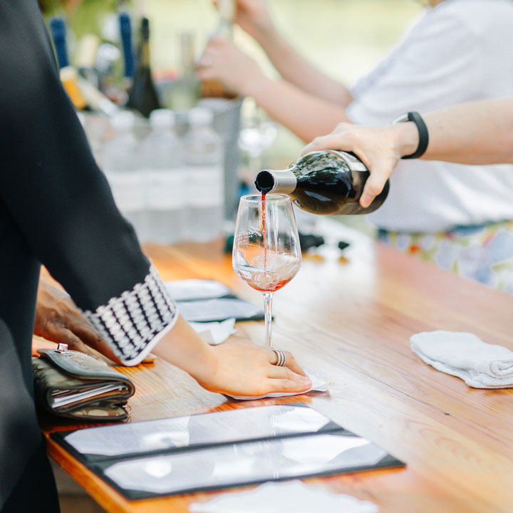 A hand with a watch pouring a glass of red wine into a stem glass at a Leesburg, Virginia winery wedding venue.