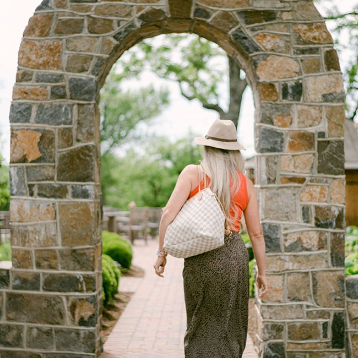 Blonde woman in a hat walking through a stone archway at Fleetwood Farm Winery, an indoor-outdoor wedding venue & winery in Leesburg, VA.